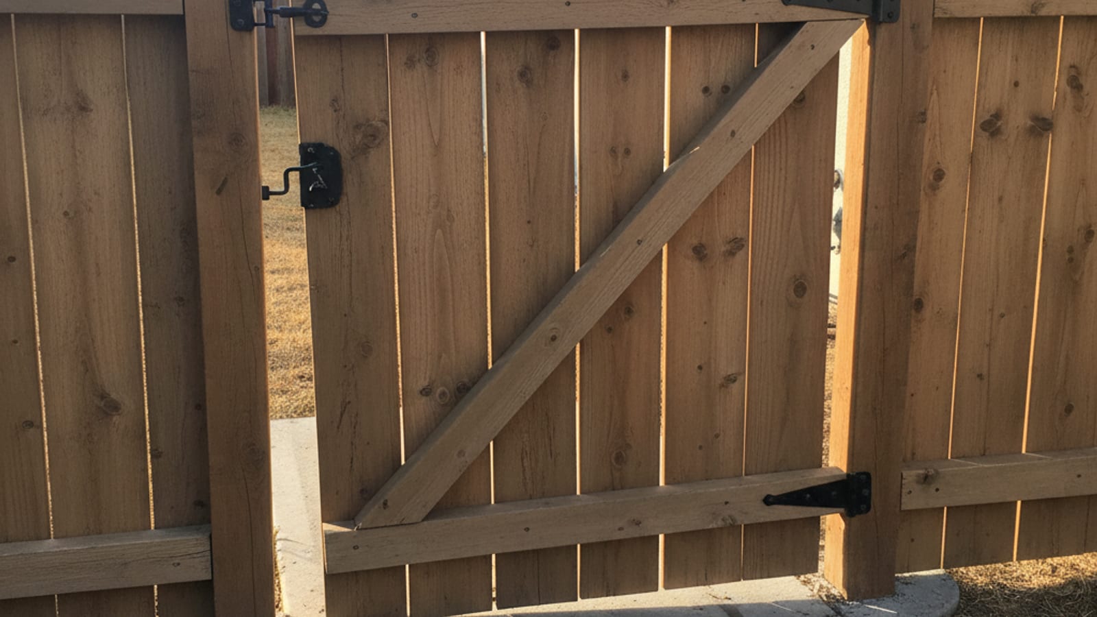 Sagging cedar fence gate dragging on concrete with a visible gap at the latch side in a San Diego side yard